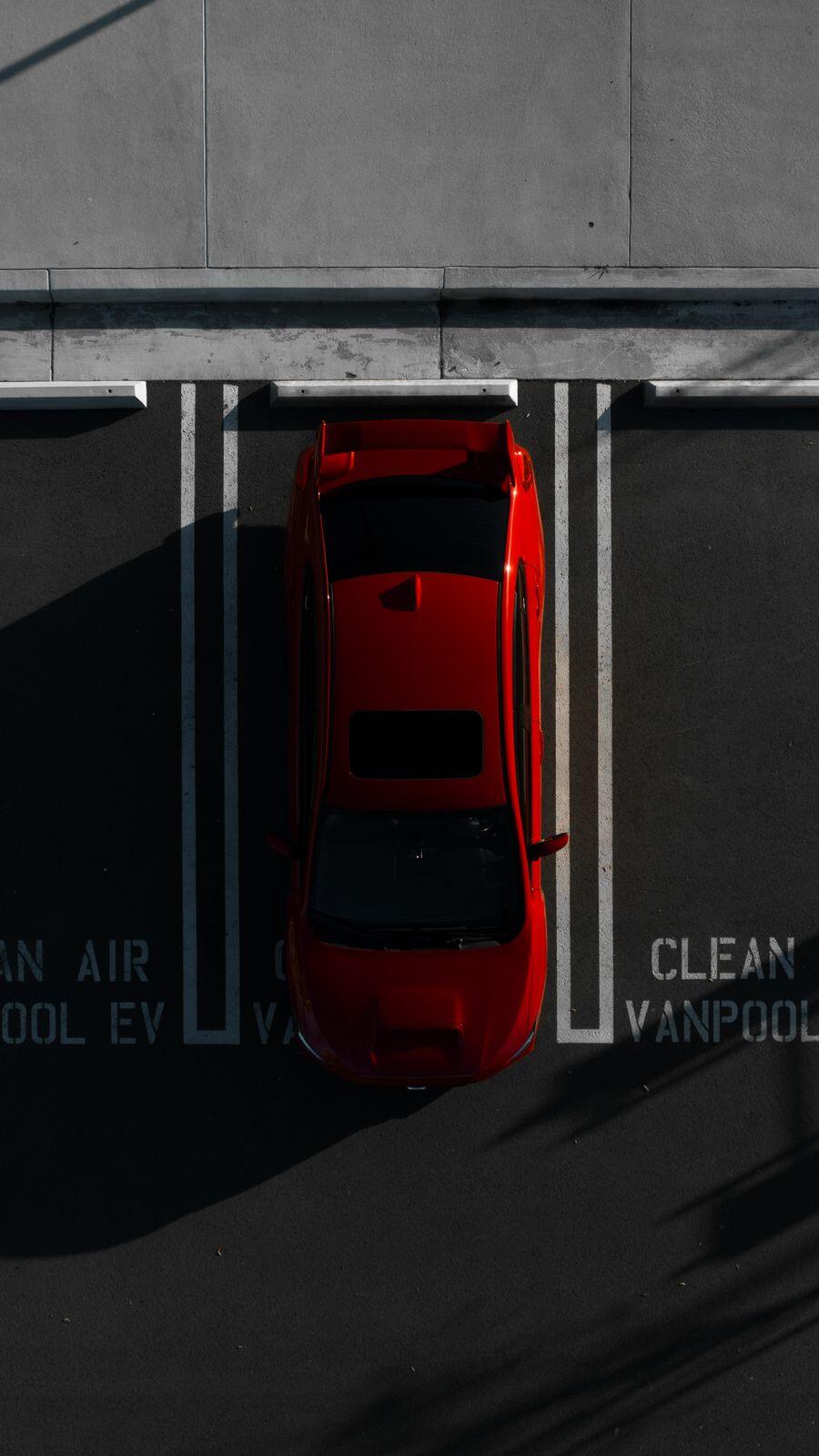 A red sedan in a concrete parking bay, seen from above
